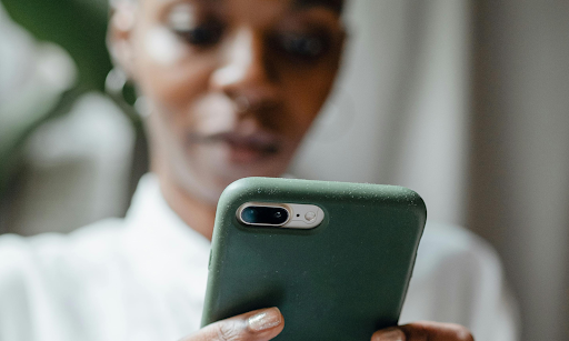 A black woman looks down at her cell phone, deeply focused. She appears to be reading something.